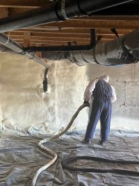 Man spraying foam insulation under a building